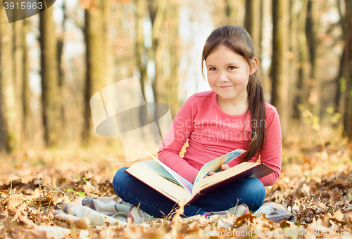 Image of Little girl is reading a book outdoors