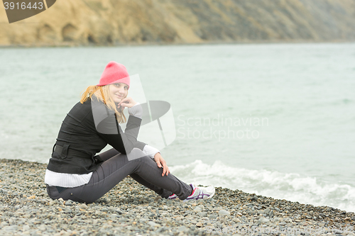 Image of Sitting on the beach on a cool cloudy day Pretty teenage girl in a pink hat