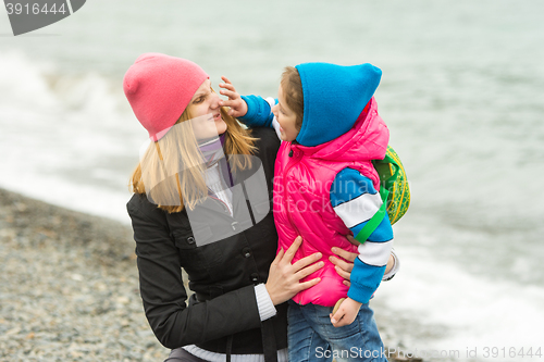 Image of Little girl having fun touches mothers nose in warm clothes on the beach