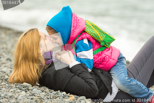 Image of Young mother lying on the pebbly seashore kissing the nose her daughter sitting on her riding