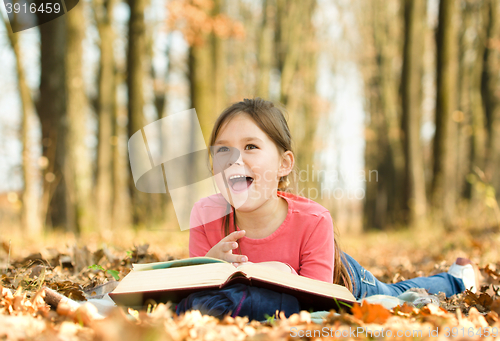 Image of Little girl is reading a book outdoors