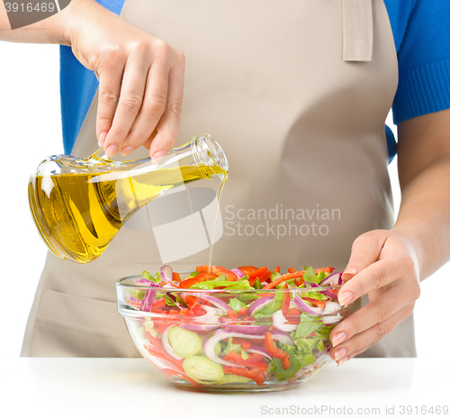 Image of Cook is pouring olive oil into salad