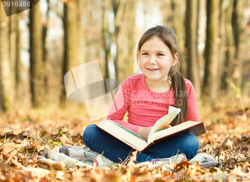 Image of Little girl is reading a book outdoors