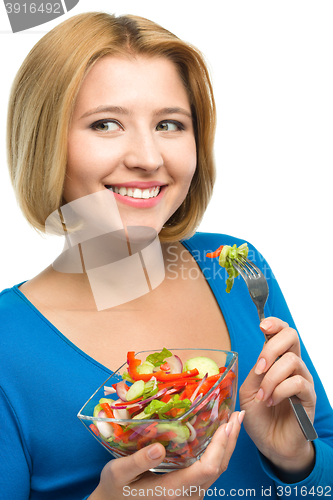Image of Young attractive woman is eating salad using fork