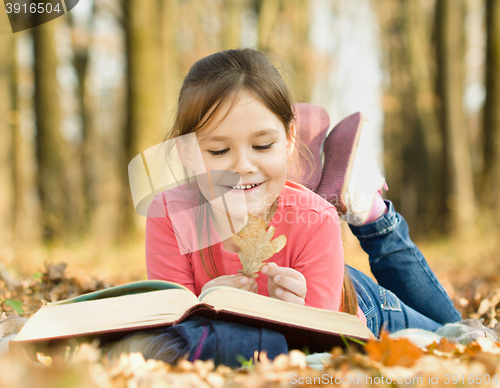 Image of Little girl is reading a book outdoors