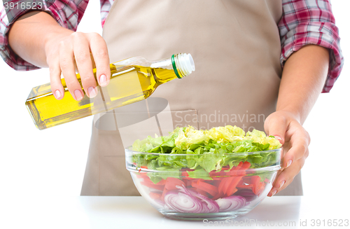 Image of Cook is pouring olive oil into salad