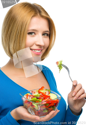 Image of Young attractive woman is eating salad using fork