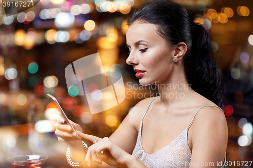 Image of young woman with smartphone at night club or bar