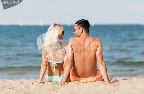 Image of happy couple in swimwear sitting on summer beach