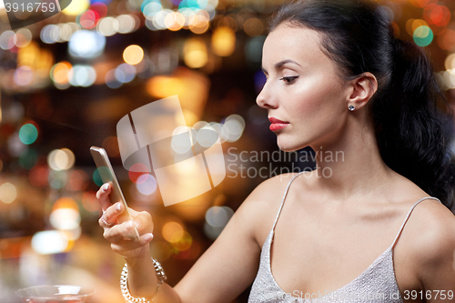 Image of young woman with smartphone at night club or bar