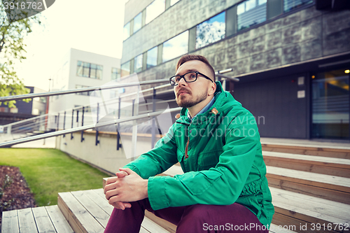 Image of happy young hipster man sitting on stairs in city