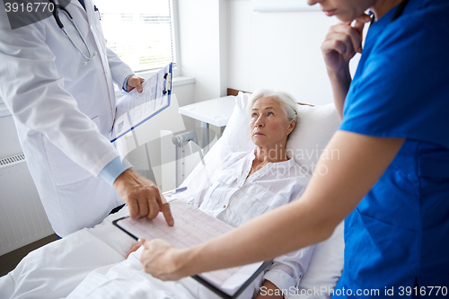 Image of doctor and nurse visiting senior woman at hospital