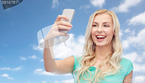 Image of smiling young woman taking selfie with smartphone