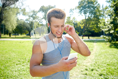 Image of happy man with earphones and smartphone at park