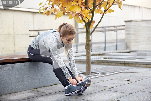 Image of happy young sporty woman tying shoelaces outdoors