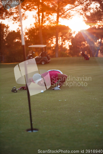 Image of golf player blowing ball in hole with sunset in background