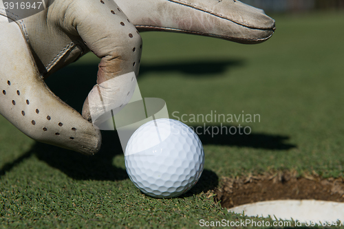 Image of man\'s hand putting golf ball in hole