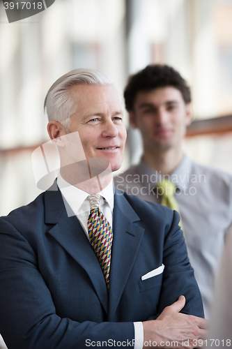 Image of portrait of senior businessman as leader  with staff in backgrou