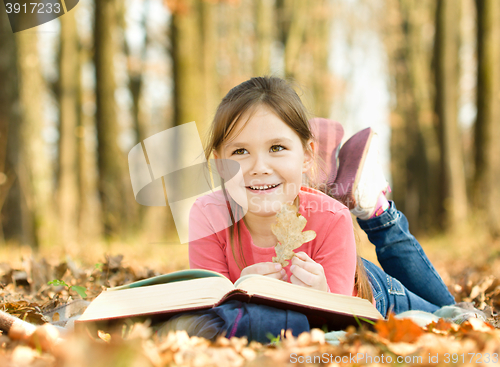 Image of Little girl is reading a book outdoors