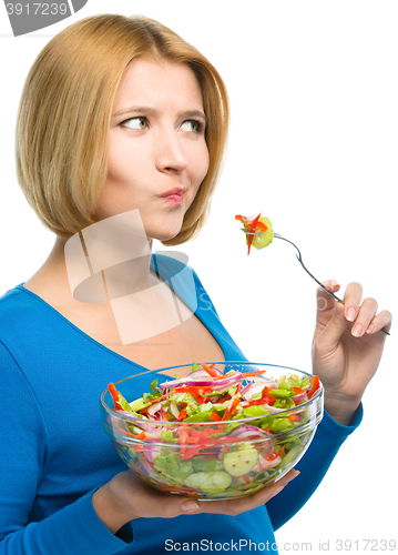 Image of Young attractive woman is eating salad using fork