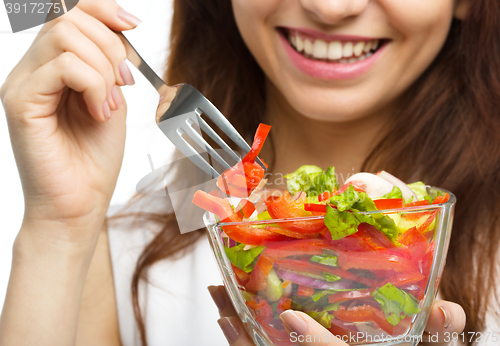 Image of Young attractive woman is eating salad using fork