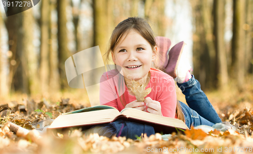 Image of Little girl is reading a book outdoors