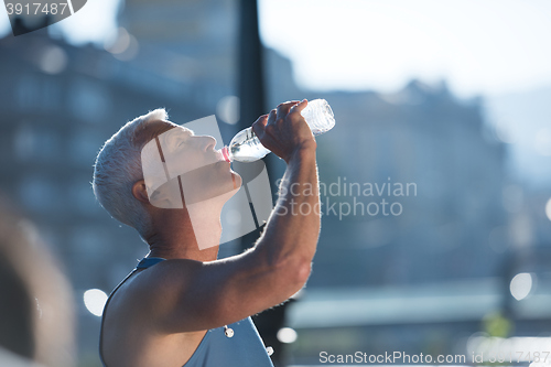 Image of senior jogging man drinking fresh water from bottle