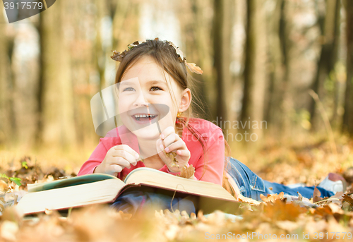 Image of Little girl is reading a book outdoors