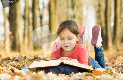 Image of Little girl is reading a book outdoors