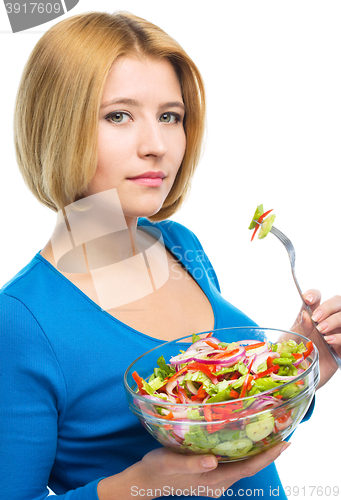 Image of Young attractive woman is eating salad using fork