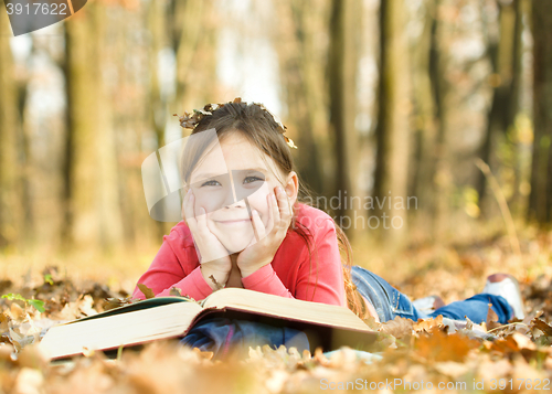 Image of Little girl is reading a book outdoors