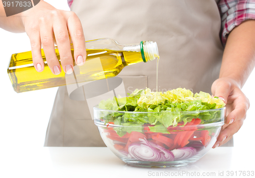 Image of Cook is pouring olive oil into salad