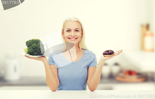 Image of smiling woman with broccoli and donut on kitchen