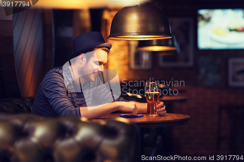 Image of man with smartphone and beer texting at bar