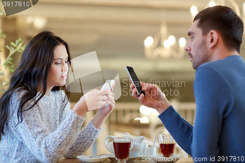 Image of couple with smartphones drinking tea at cafe