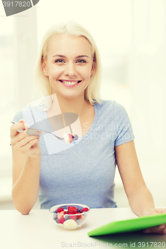 Image of smiling woman eating fruits with tablet pc at home