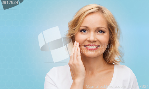 Image of smiling woman in white t-shirt touching her face