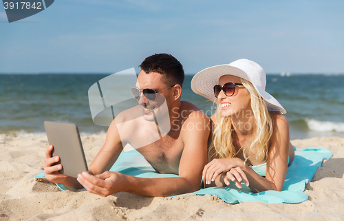 Image of happy couple with tablet pc sunbathing on beach