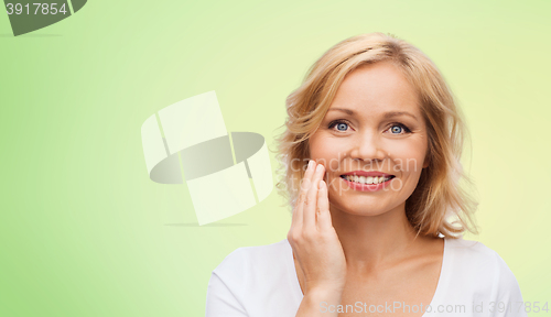 Image of smiling woman in white t-shirt touching her face