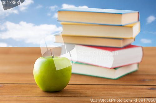 Image of close up of books and green apple on wooden table