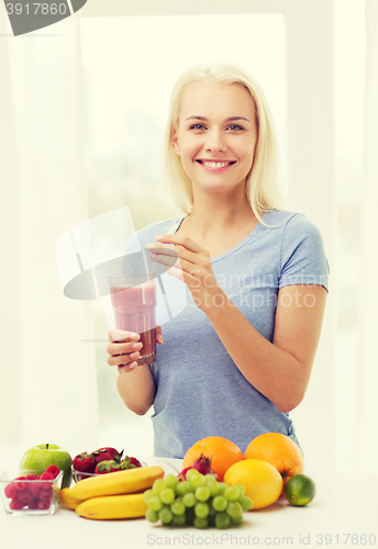 Image of smiling woman drinking fruit shake at home