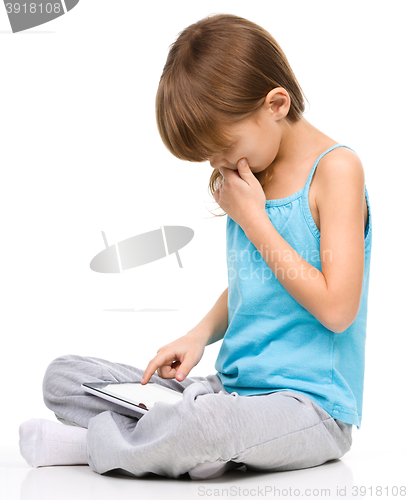 Image of Young girl is using tablet while sitting on floor
