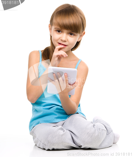 Image of Young girl is using tablet while sitting on floor