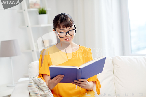 Image of smiling young asian woman reading book at home