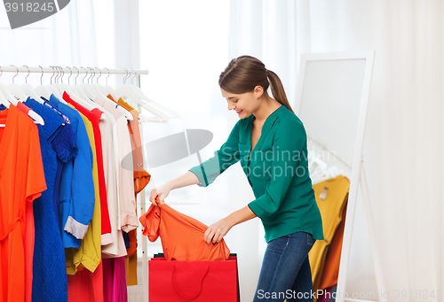 Image of happy woman with shopping bags and clothes at home