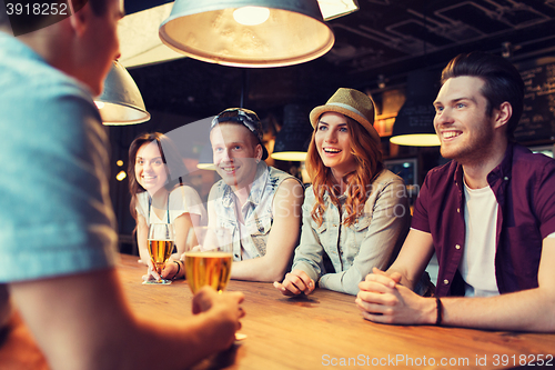 Image of happy friends drinking beer and talking at bar