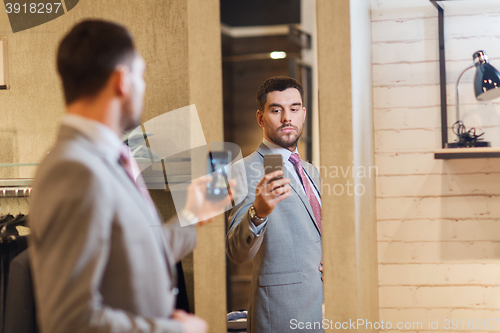 Image of man in suit taking mirror selfie at clothing store