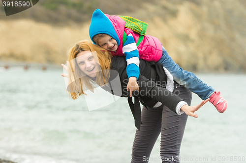 Image of Young girl having fun ride on the back of a little girl on the shore in cold weather