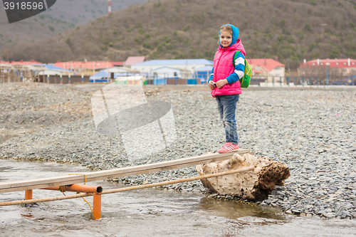 Image of  A five-year girl is undecided at the end of the plank thrown across a stream