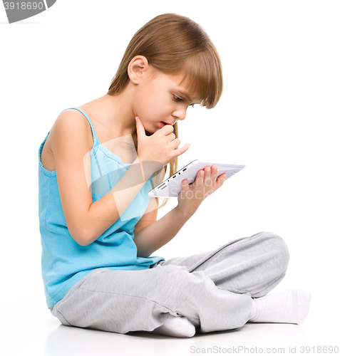 Image of Young girl is using tablet while sitting on floor